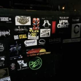 More band stickers are posted on the wall of John's sound booth area.