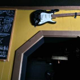 A signed guitar hangs above the frame of a doorway, next to a bar specials board.